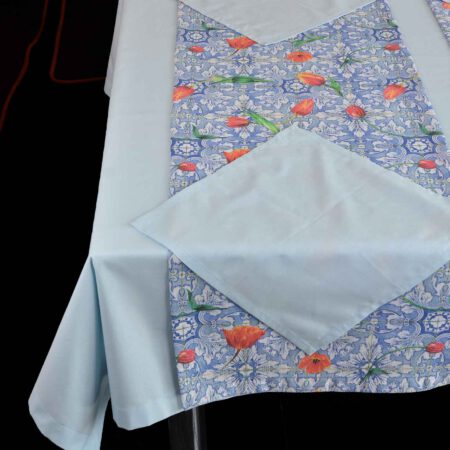 Част от маса със светлосиня покривка, платнеи салфетки и тишлайфер в разцветка с червени лалета