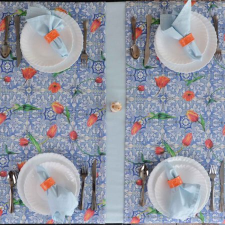 Изглед отгоре на маса сервирана със сини покривка, тишлайфери и салфетки, прибори и бели чинии